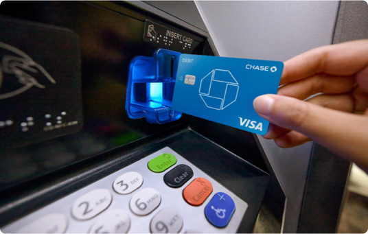 A hand inserts debit card into a Chase ATM machine to withdraw money
