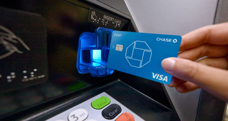 A hand inserts debit card into a Chase ATM machine to withdraw money